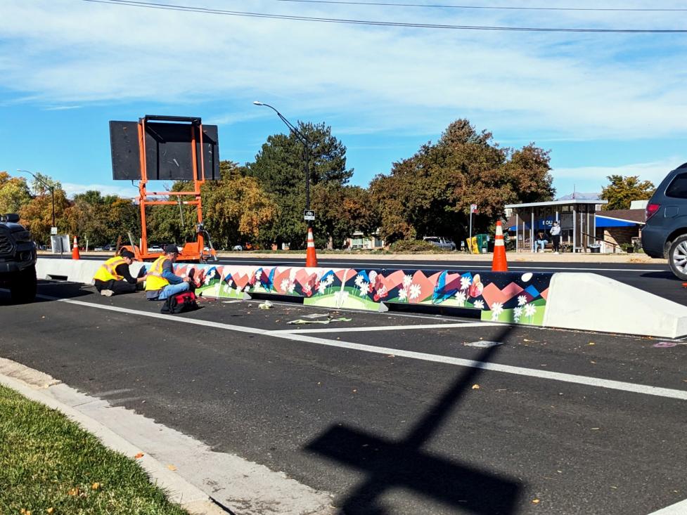 People installing murals by artist Talia Swartz Parsell on tall concrete curbs at Baseline Road