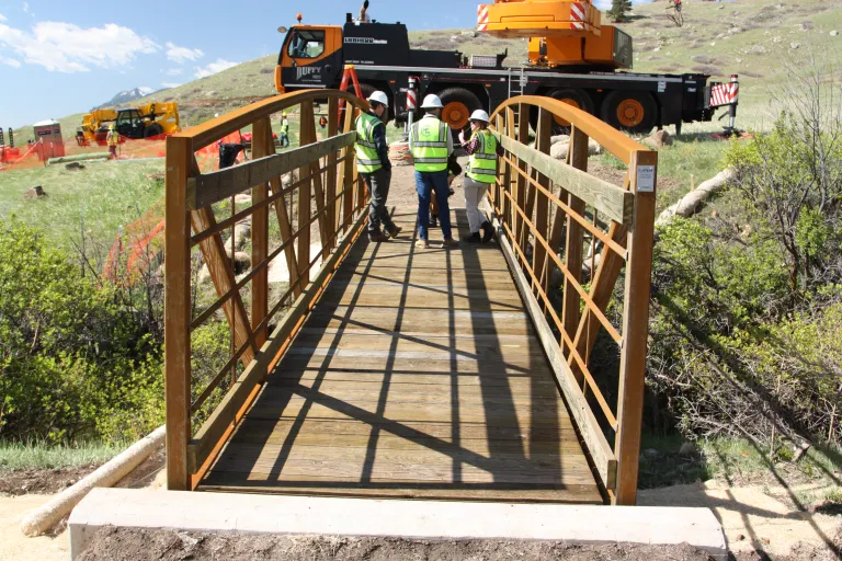 Three construction workers stand on the newly placed metal bridge over Schneider Draw on North Sky Trail