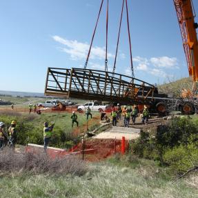 A large crane lowers a metal bridge over Schneider Draw to connect the North Sky Trail