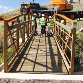 Three construction workers stand on the newly placed metal bridge over Schneider Draw on North Sky Trail