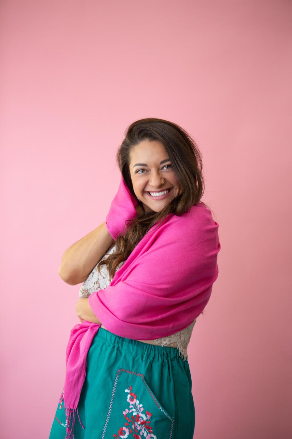 Maya Sol smiling at the camera wearing a bright pink shawl and turquiose skirt.