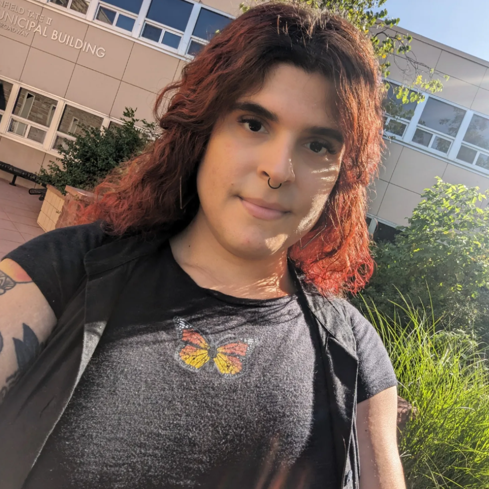 Selfie of Ruby Sofia Lopez smiling and wearing a dark grey shirt with a butterfly.