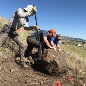 Three volunteers moving a large rock off a trail