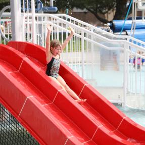 Girl sliding down the red slide at Scott Carpenter Pool