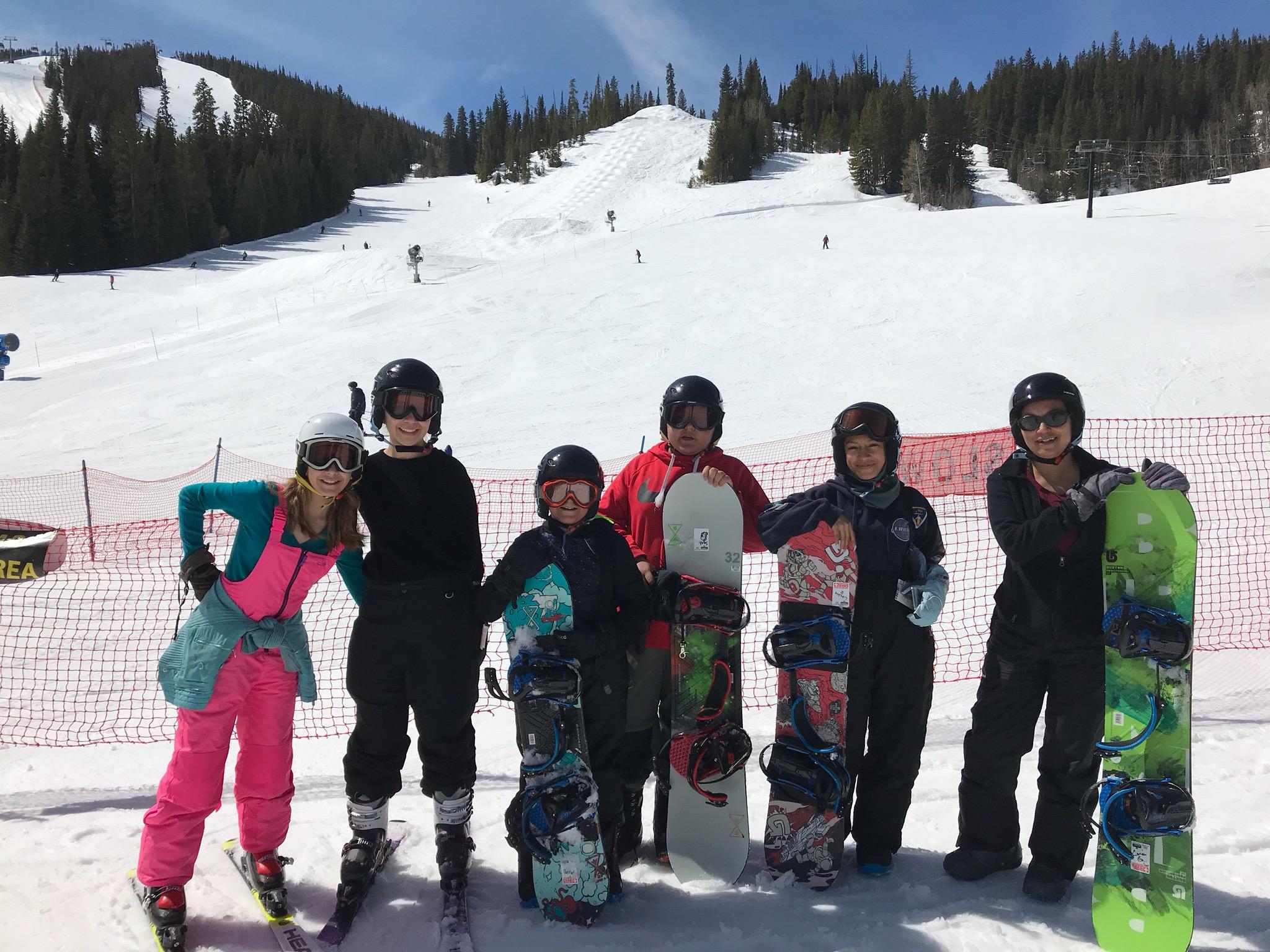 A group of kids pose with their snowboards in front of a ski hill.