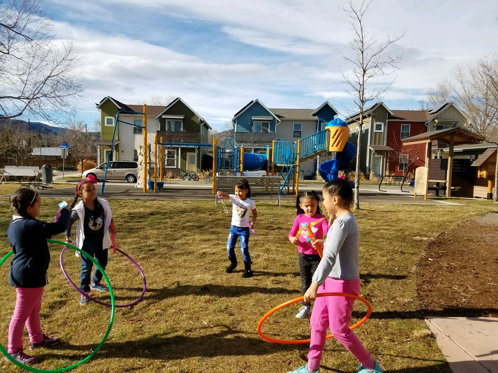 A group of girls play with hula hoops in front of a playground.