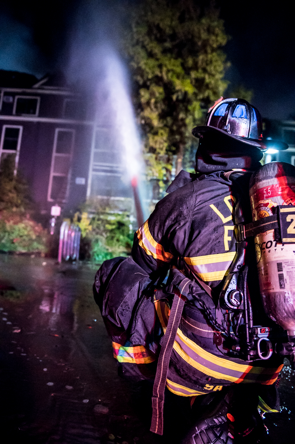 Firefighter holding hose toward apartment fire.