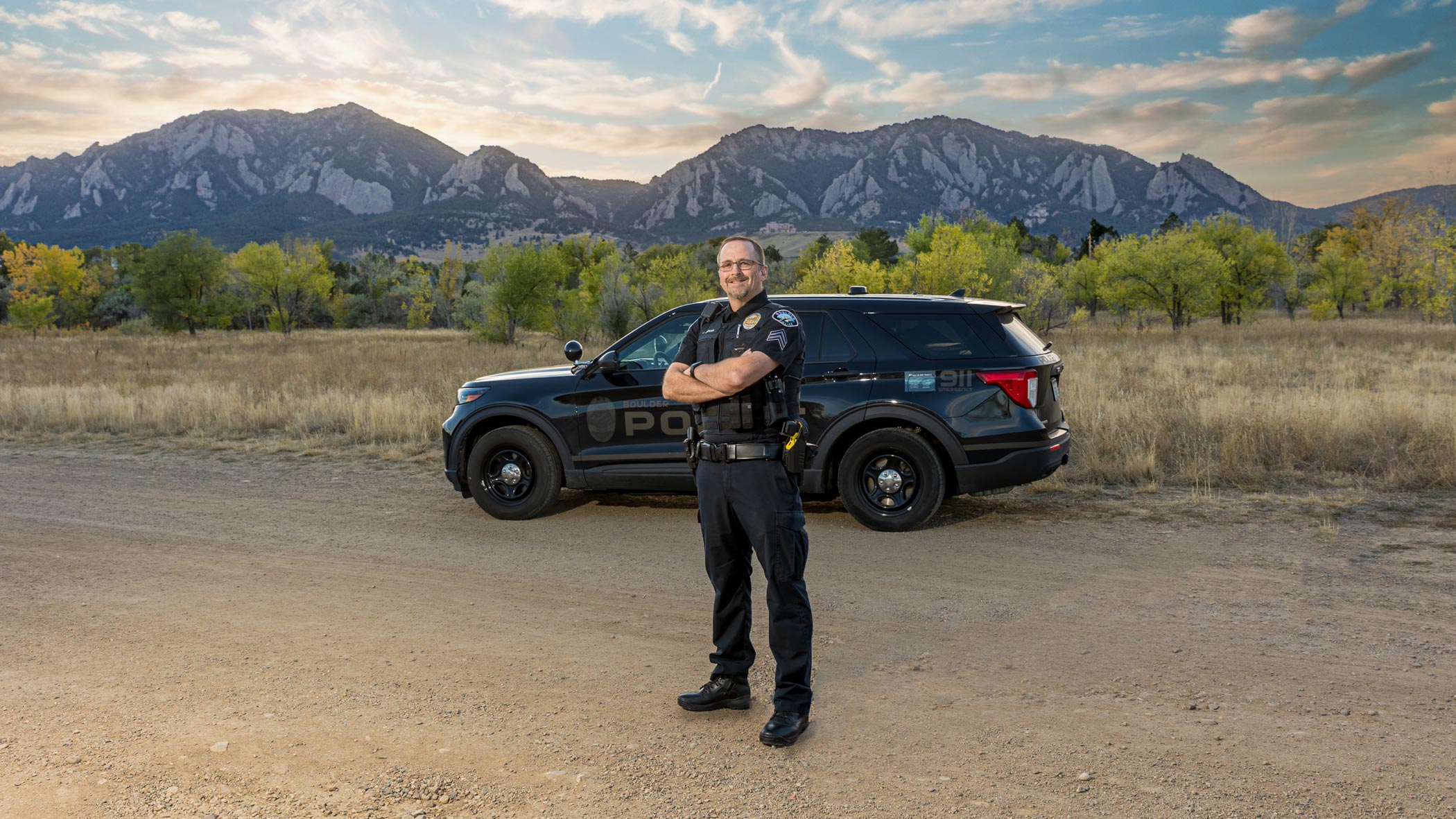 Boulder PD officer posing in front of vehicle with mountain backdrop.
