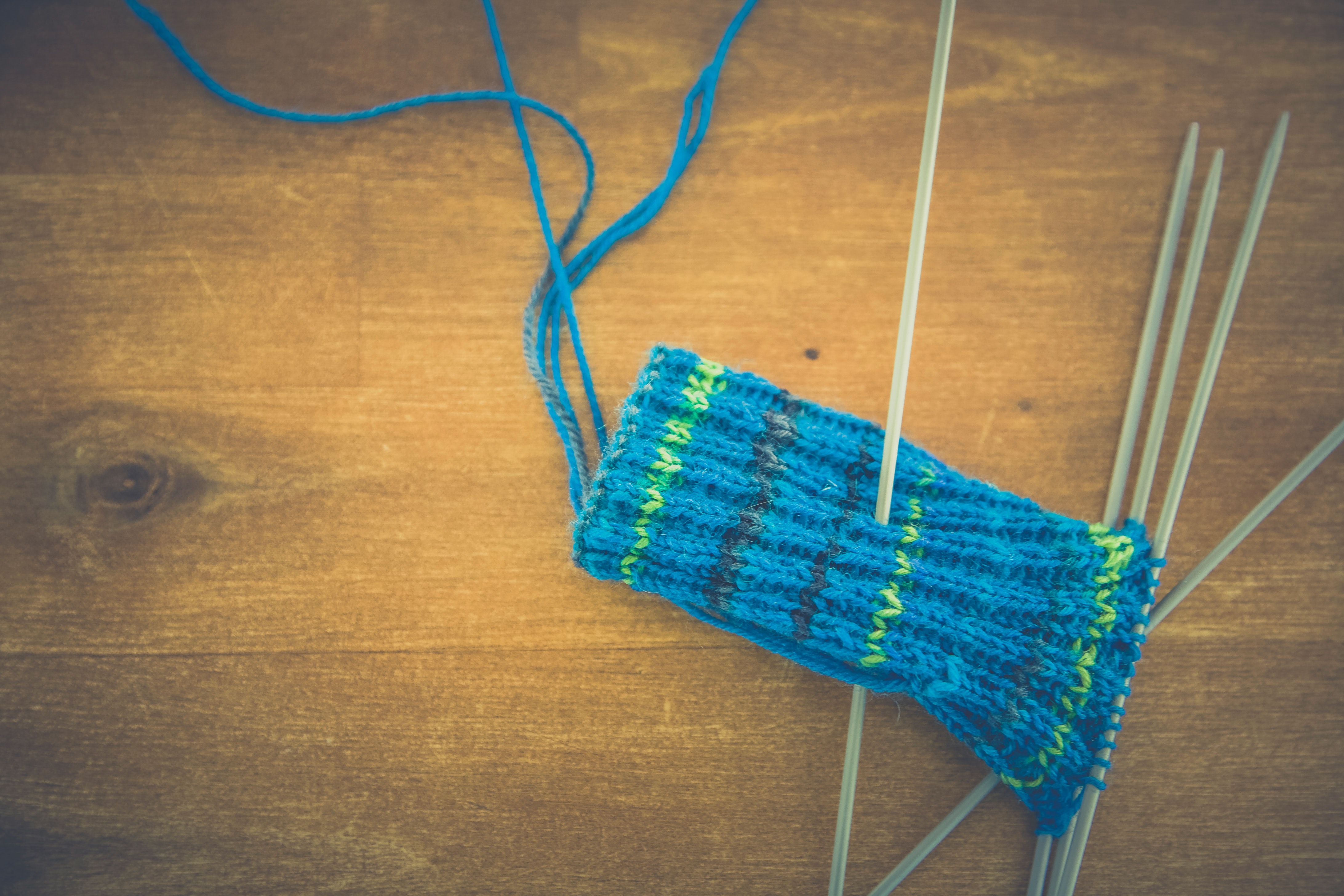 Half-knit blue mitten with knitting needles