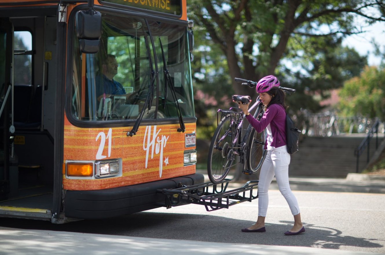 A person putting a bike onto a bike rack on a bright orange bus.