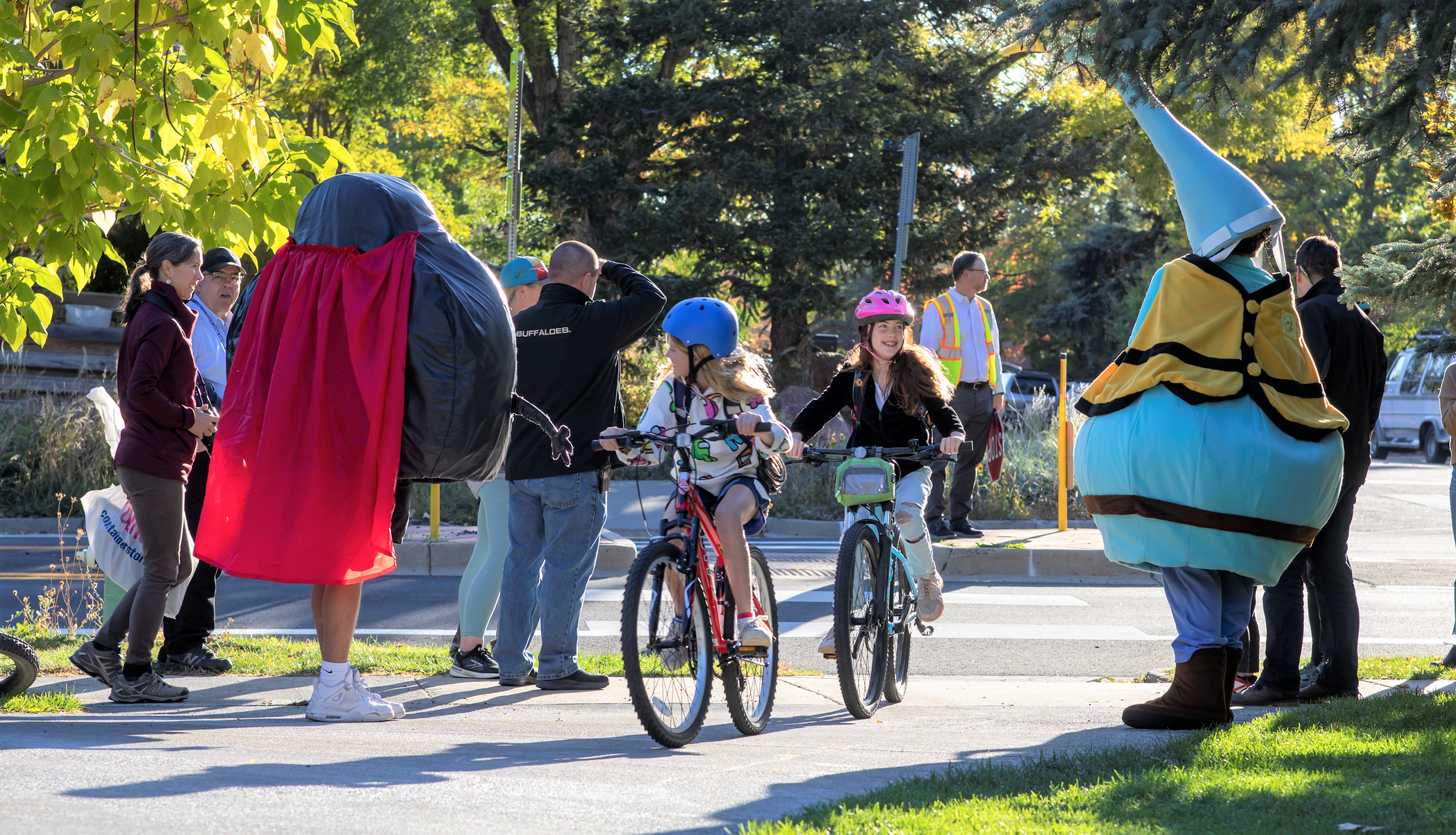 Children smiling and biking down a multi-use path next to costumed traffic safety mascots