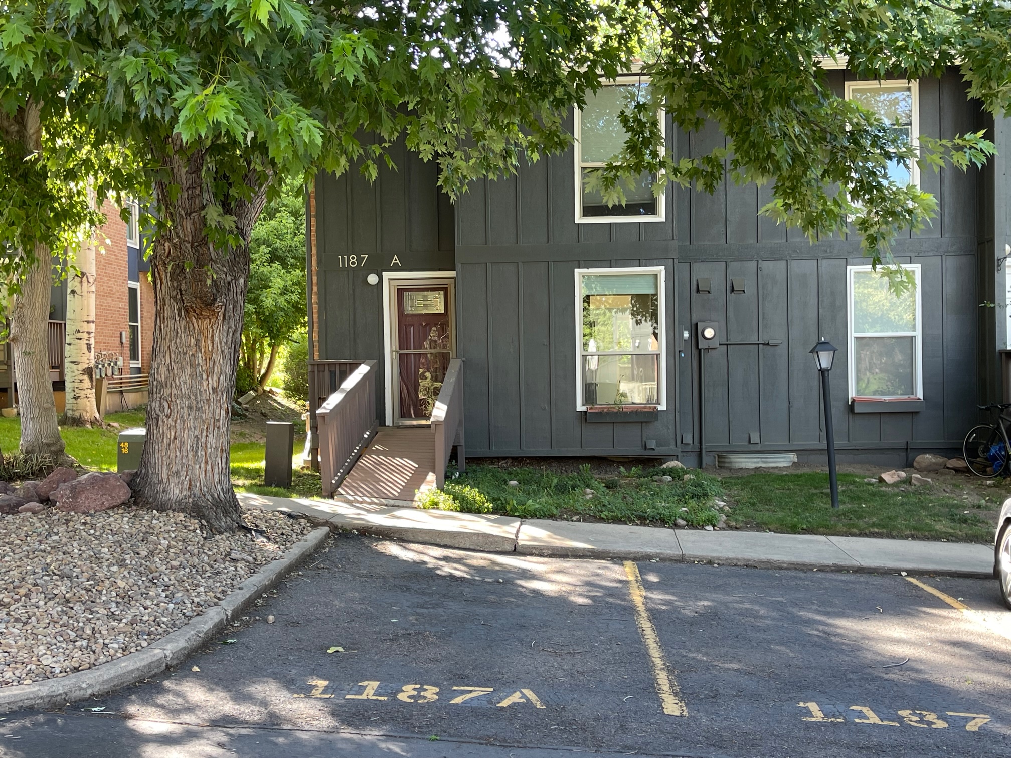 Condo front with two parking spaces and tree with green leaves
