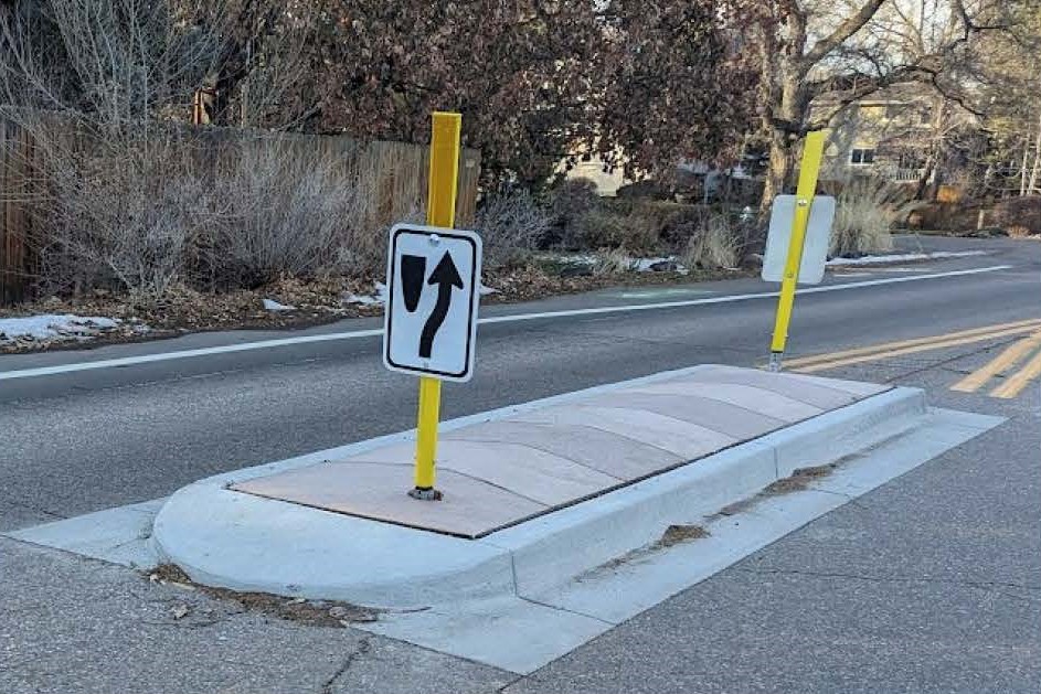 An example splitter island, or traffic calming device, on 26th Street. It is a raised area of concrete in the middle of the road. On the island is a traffic sign showing vehicles to travel to the side of the island. 