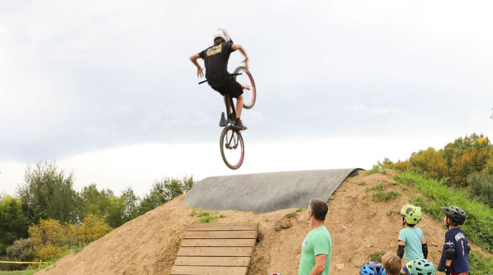 A teen on a mountain bike getting air time over a hill at Valmont Bike Park as onlookers watch