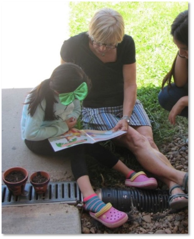A volunteer reads with a young child in the grass