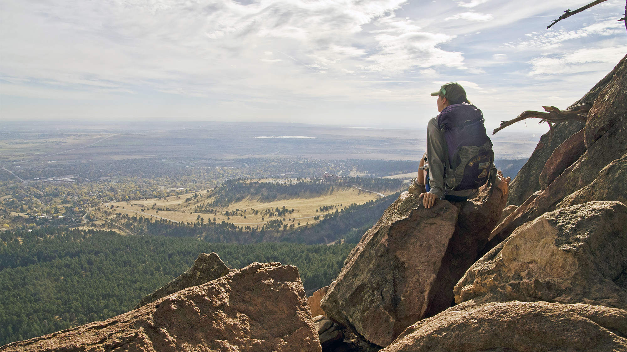 A woman sits on a cliff formation on open space high above Boulder