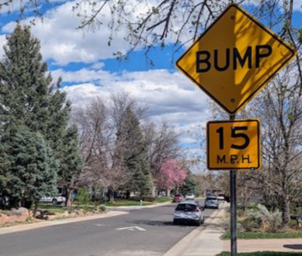 Yellow caution sign alerting vehicles of a speed bump ahead on Floral Drive with a speed limit of 15 miles per hour. 