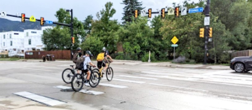 Three school-aged children commuting by bike through a crosswalk at an intersection.  
