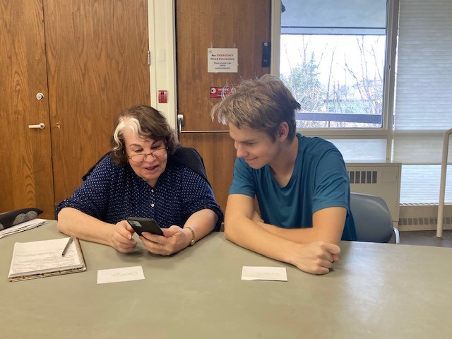 A high school student helps an older adult with their mobile phone