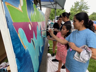 People of all ages stand next to a large canvas painting bright colors.