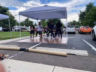 Men dance on a stage under a tent in a parking lot. 