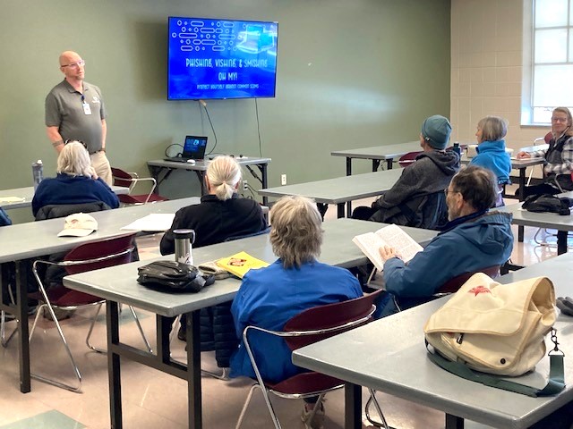 Older adults are in a classroom, receiving education about staying safe online.