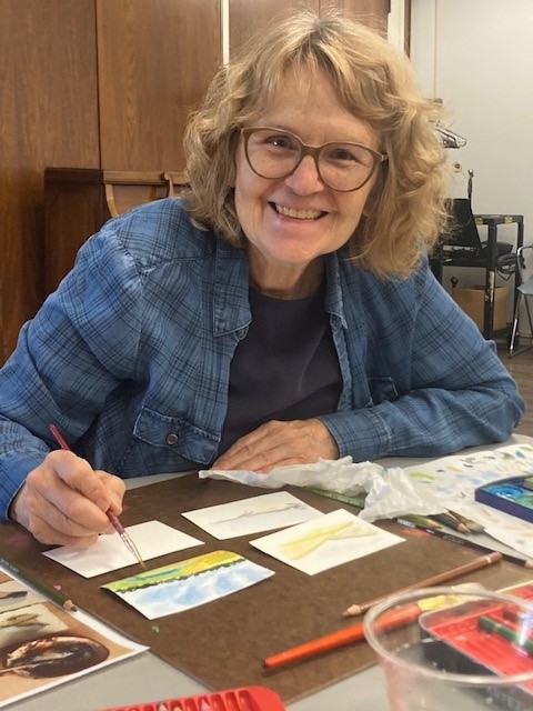 A woman is smiling while painting with watercolors.