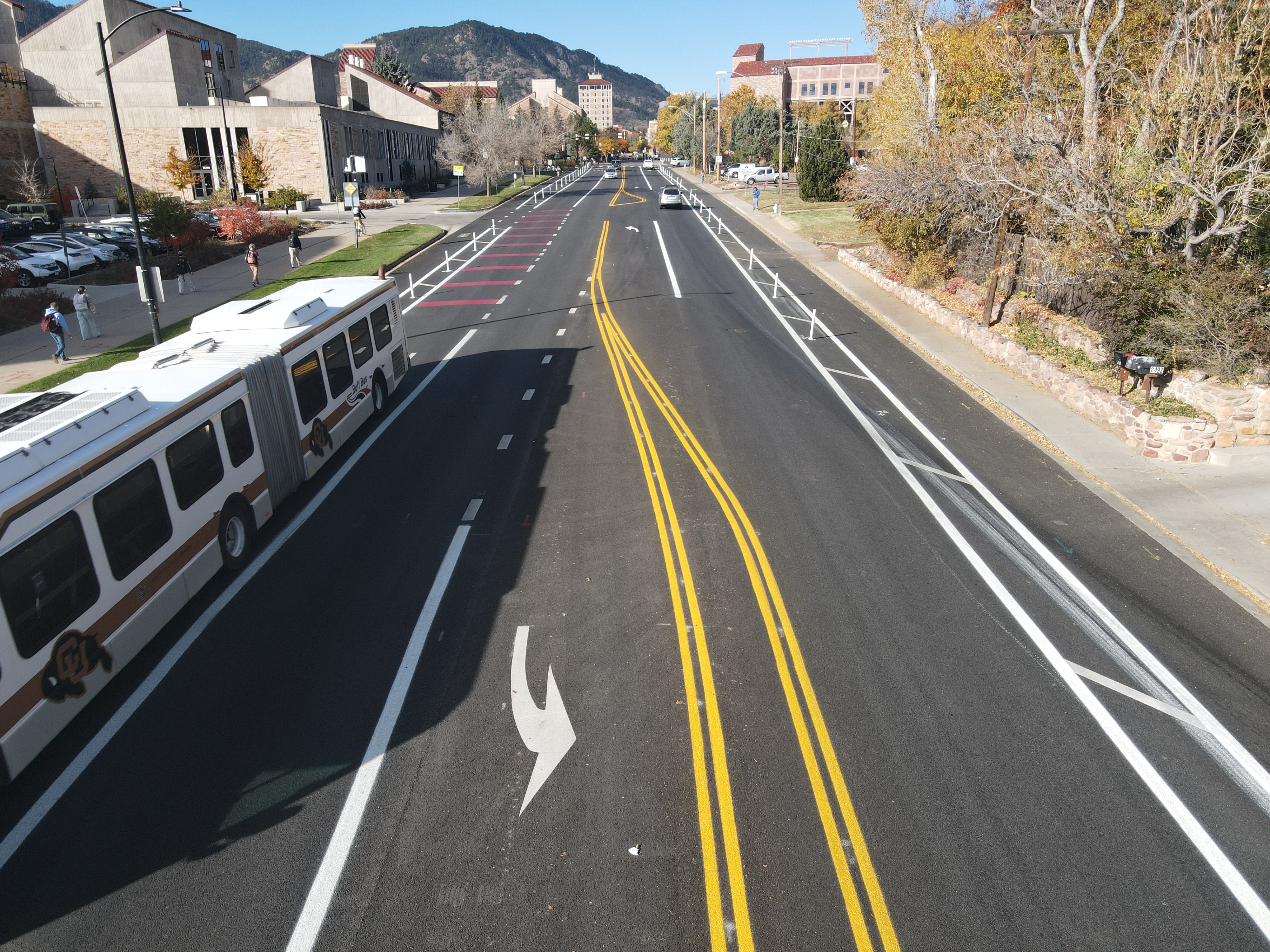 After 2025 mobility enhancements, a CU Boulder Buff Bus travels eastbound on Colorado Avenue west of Regent Drive in the bus lane, which is marked with red pavement markings.