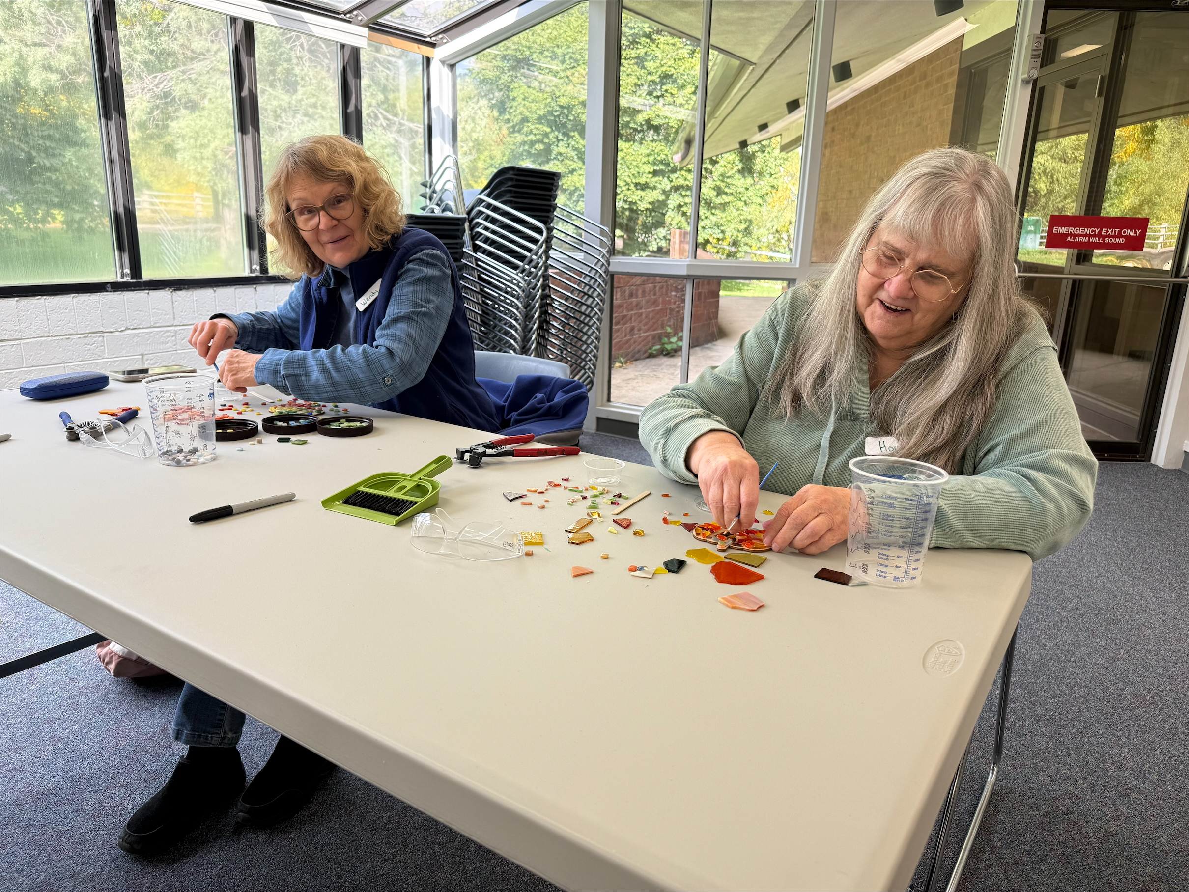 Two OAS clients sit at a table working on mosaic arts crafts. 