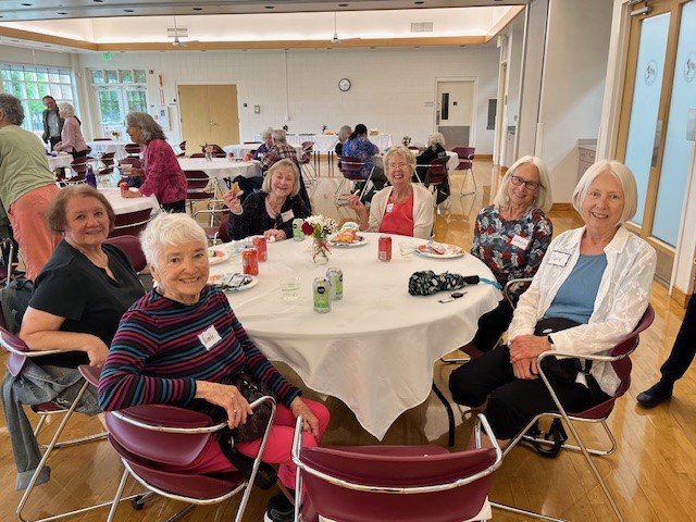 A group of women are sitting at a round table and smiling at the camera.