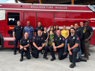 Fire fighters and community members sitting and standing in front of a bright red fire engine