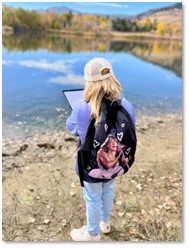 A child holding a notebook looking out at a pond.
