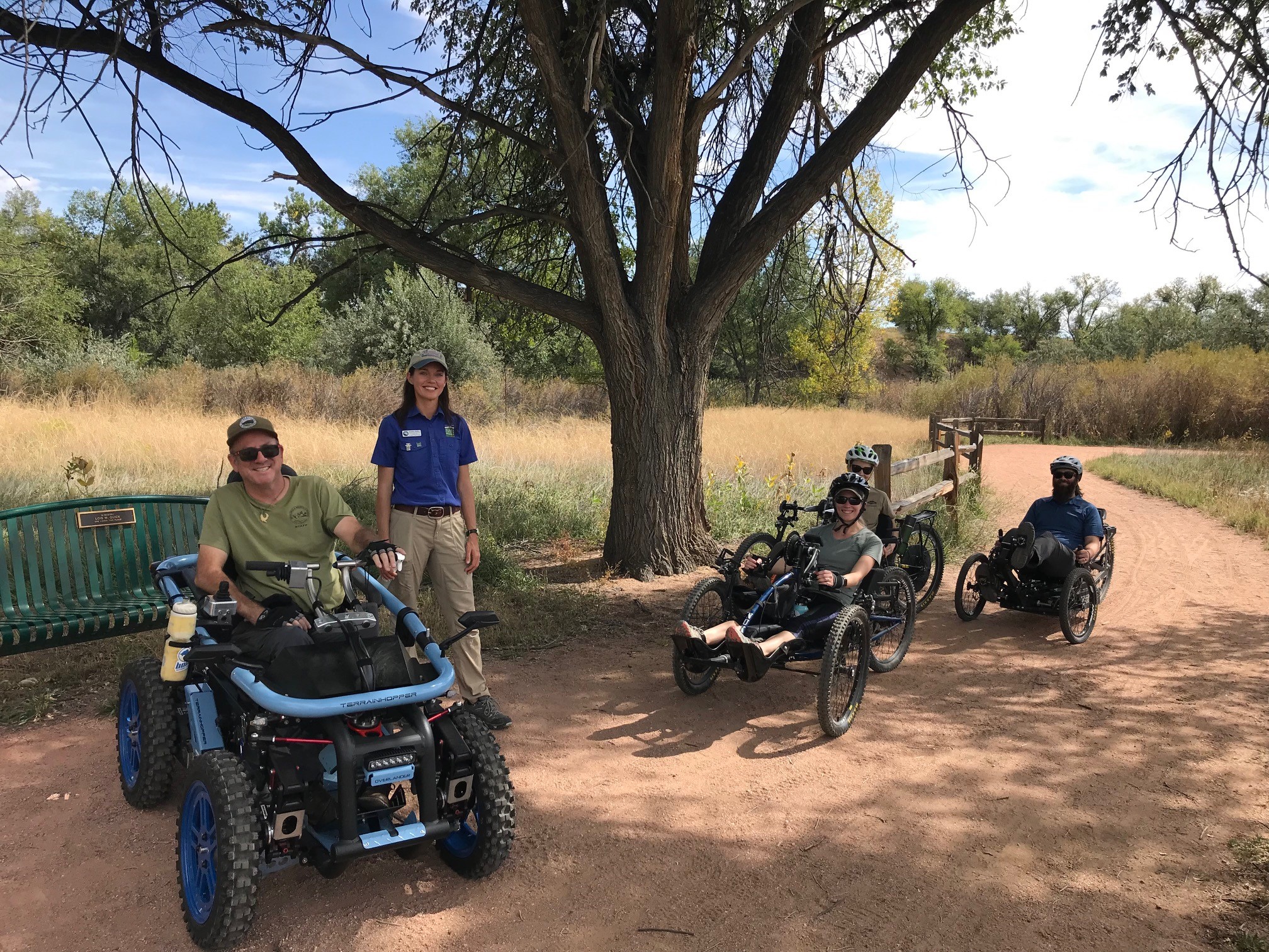 Group of people on a dry trail outside in accessible hand bikes and on a terrain hopper.