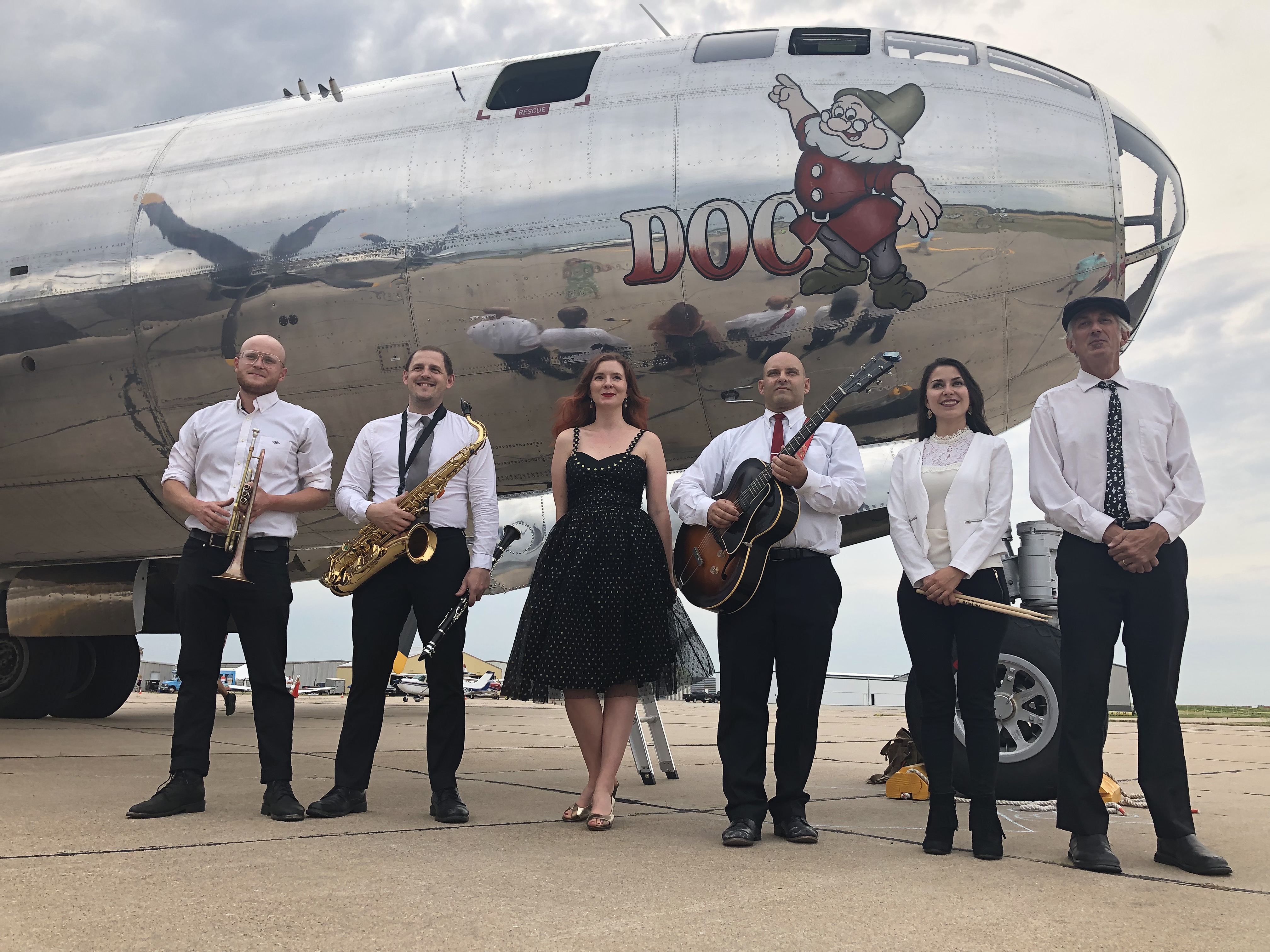 Dizzy with a Dame band members posing in front of plane. 