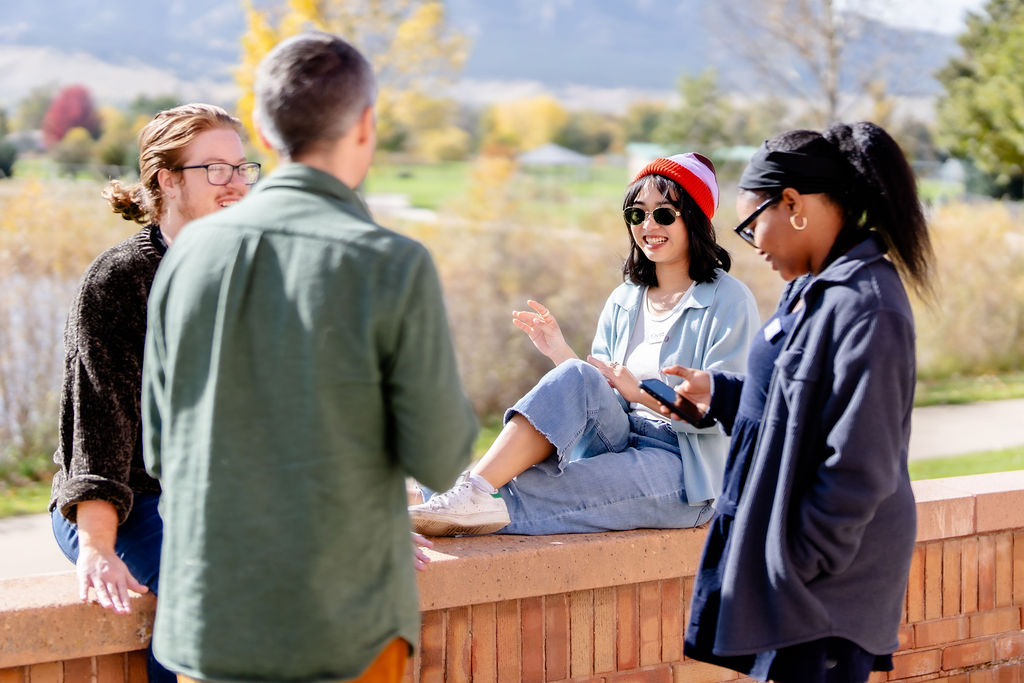Four young adults sitting and standing in a circle talking with each other. 