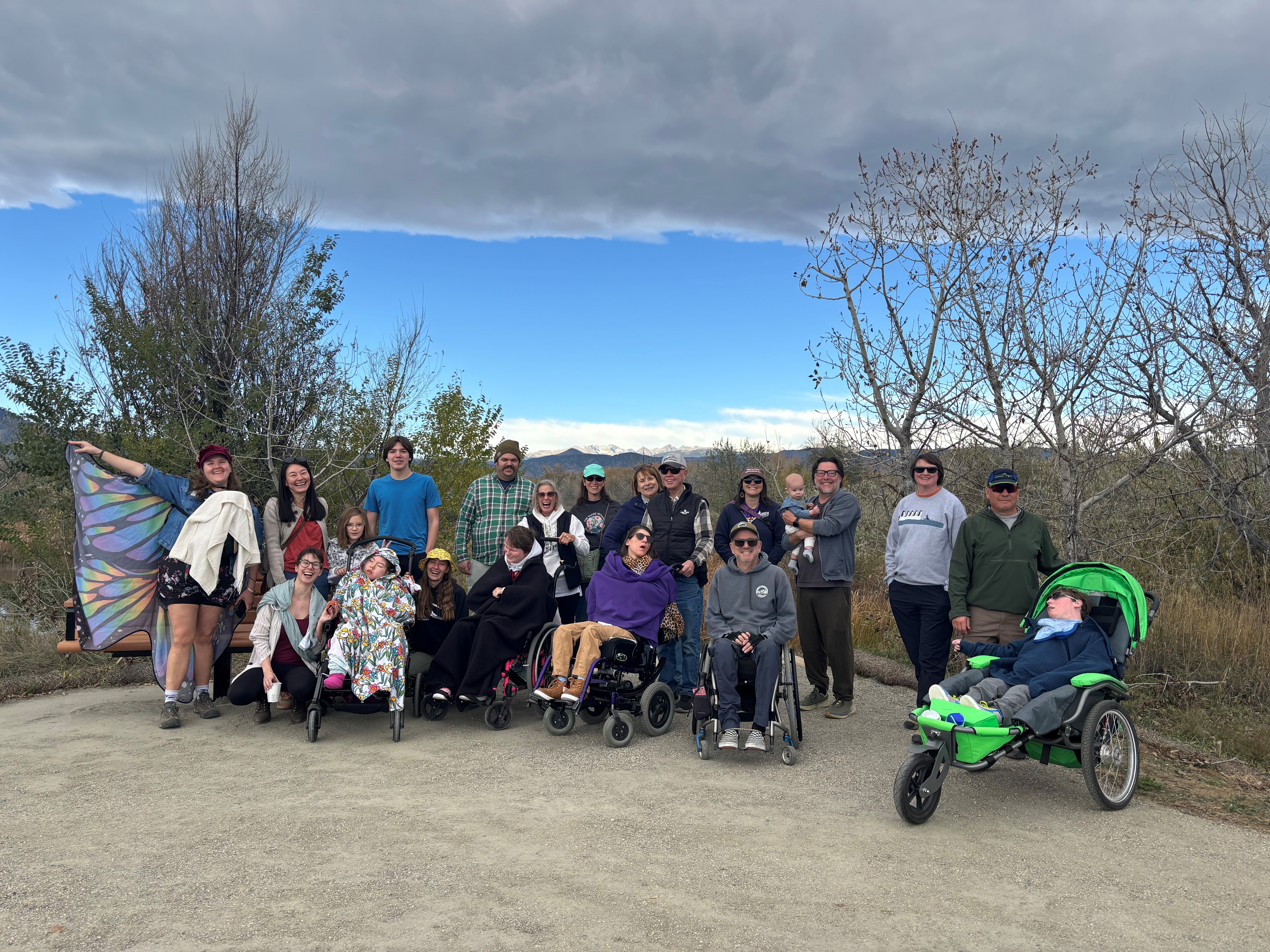 Group of people standing next to a lake, multiple young children in wheelchairs.