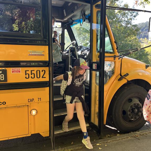 Small children exit a yellow school bus.