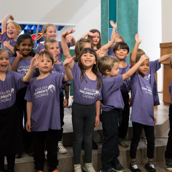 Children waving and smiling who are part of a children's chorale