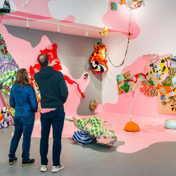Attendees of an art exhibit looking at colorful art on walls