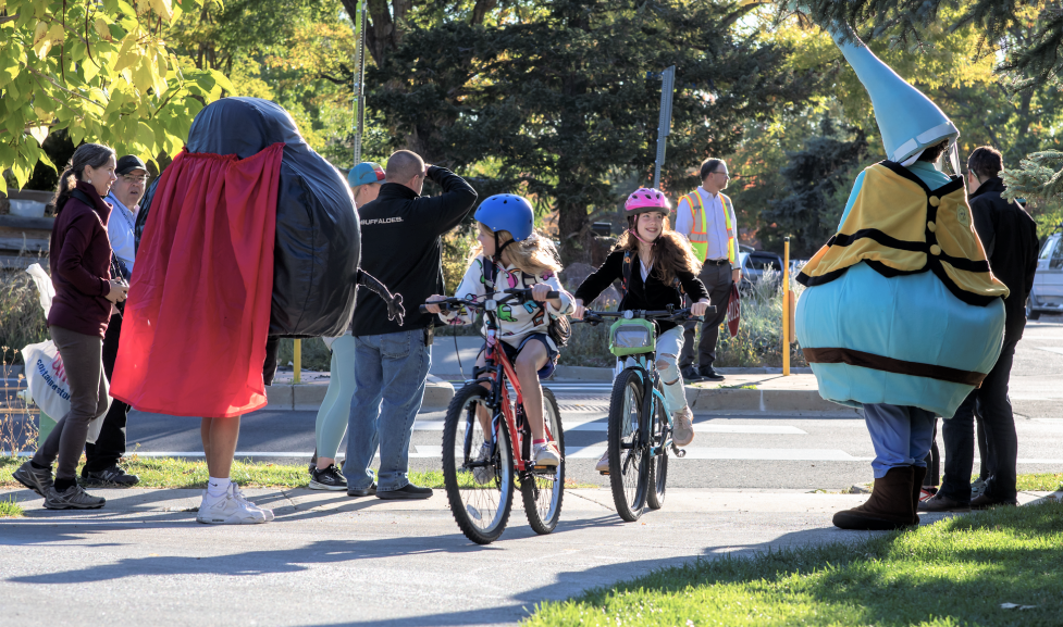 Kids biking and smiling at BVSD mascots. 