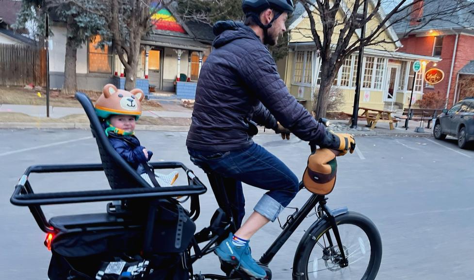 A person biking on an e-cargo bike with a child in the backseat