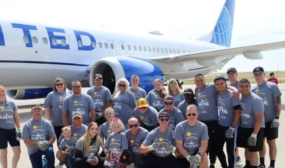 Boulder Police Department staff and family and friends posing happily in front of an airplane