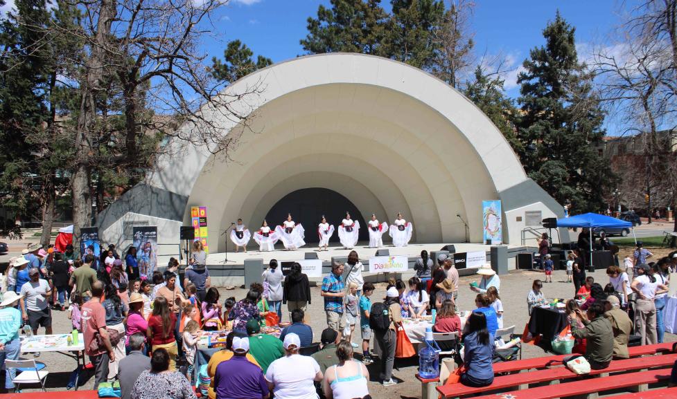 Spanish dancers in costume perform in the bandshell as an audience watches from the outdoor seating aisles 