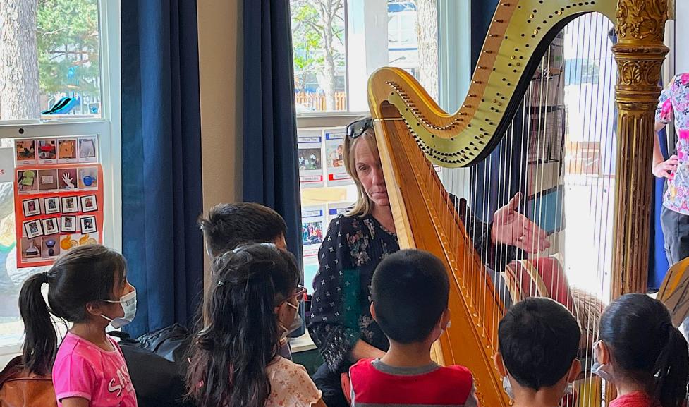 A female harpist plays as elementary aged kids watch and listen