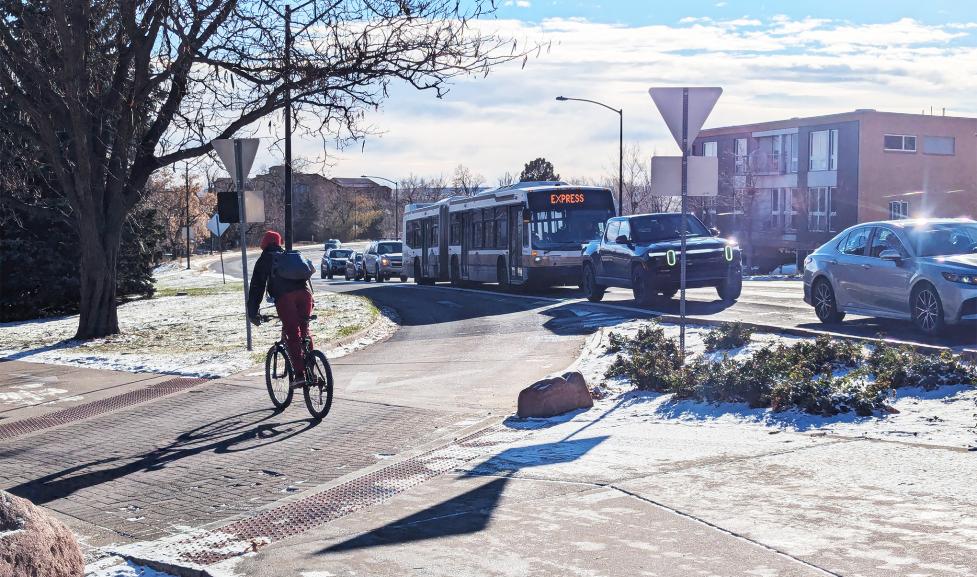 Person biking across crosswalk near Broadway while express bus and cars line up at traffic signal