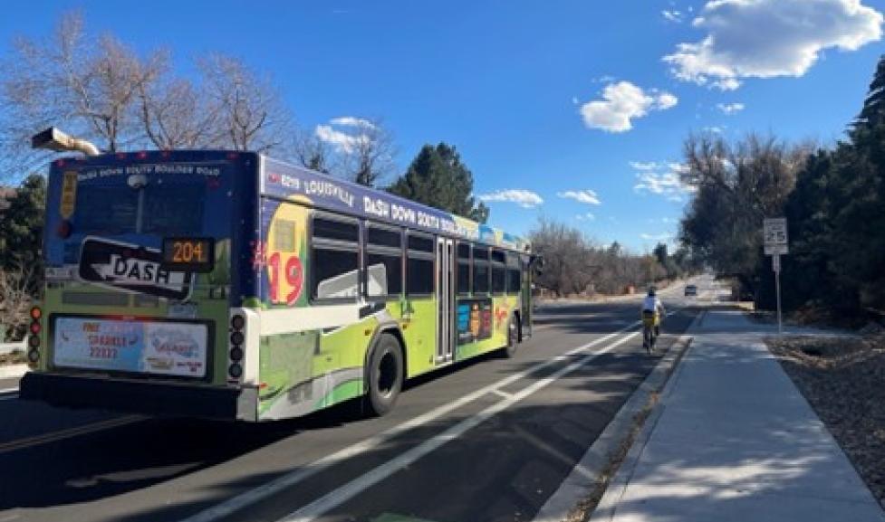 bus driving on road next to person biking besides buffered bike lane and sidewalk