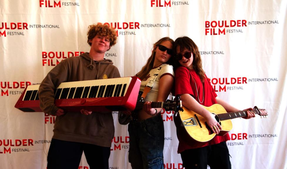A teenage boy and two teenage girls pose holding a piano and two guitars, respectively 
