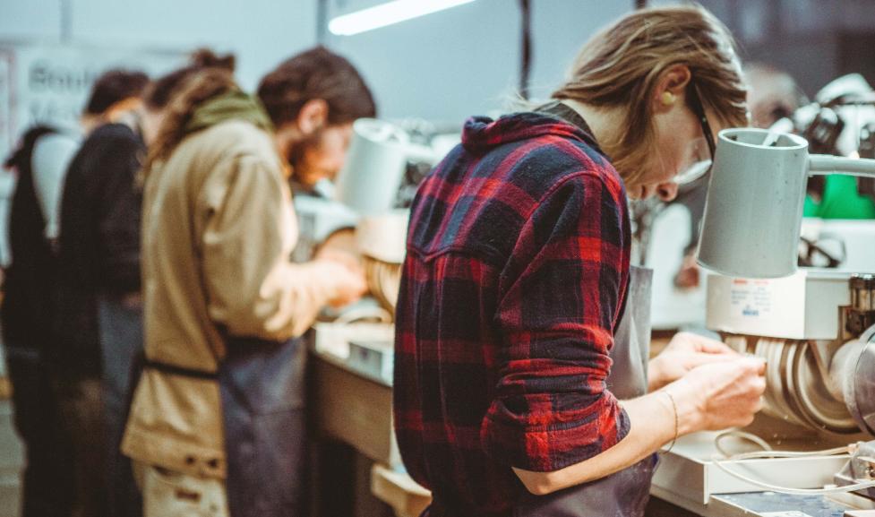Four young white students work on metalsmithing, facing away from the camera