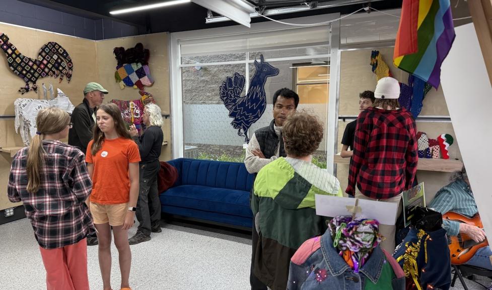Ten teenagers gather in a gallery communal room with a pride flag and artwork on the walls 