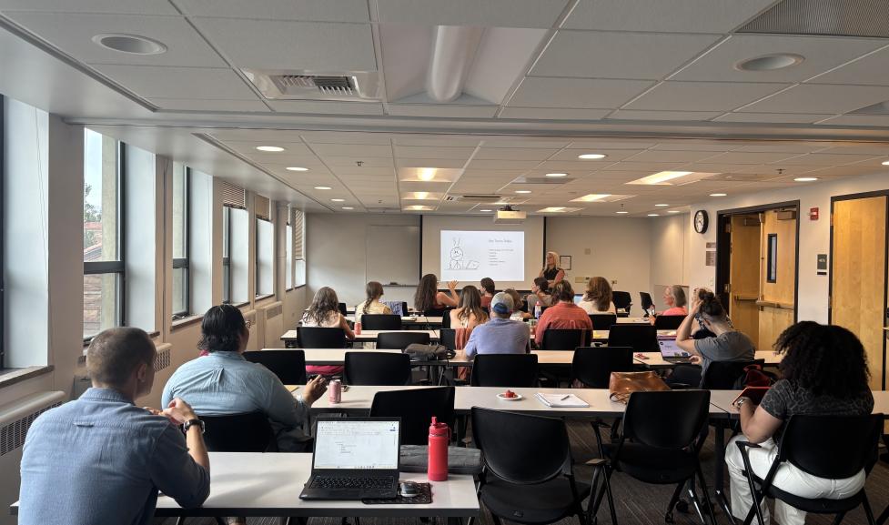 About twenty people sit in rows watching a woman give a powerpoint presentation on grant writing